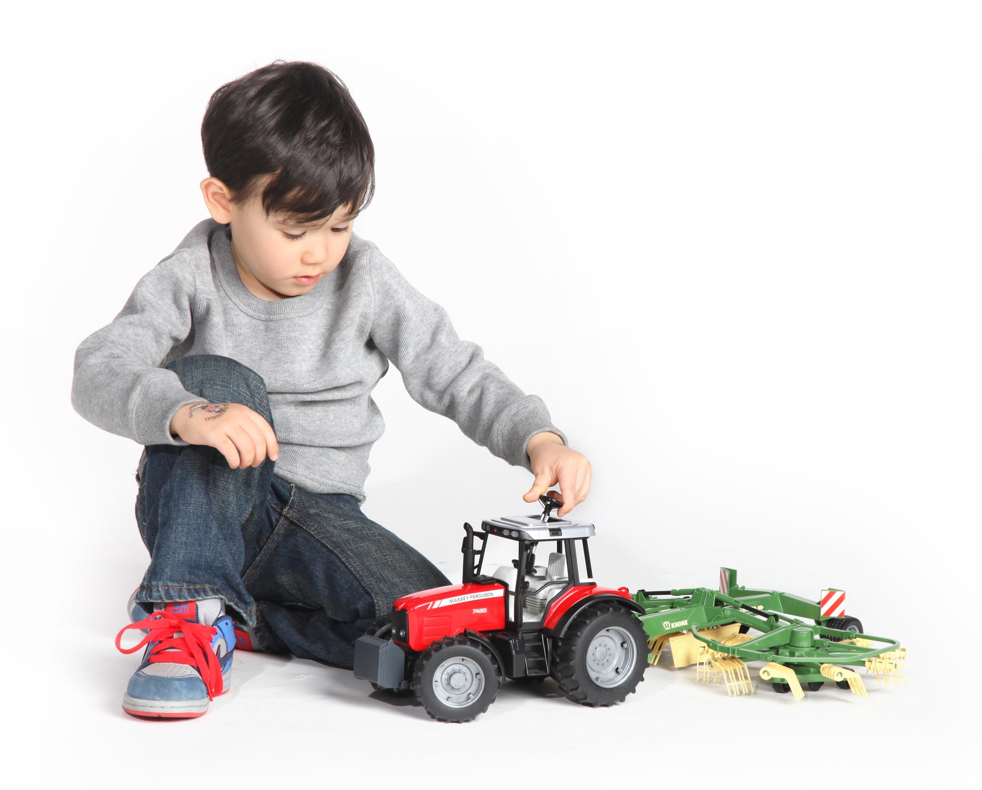 Child playing with red toy tractor and green swath windrower from Vehicles & Remote Controlled Toys collection