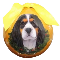 Tri-color King Charles dog portrait on Christmas ball ornament with yellow bow and holiday wreath design