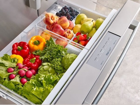 Open bottom freezer drawer showing organized fresh vegetables and fruits in glass and stainless steel compartments