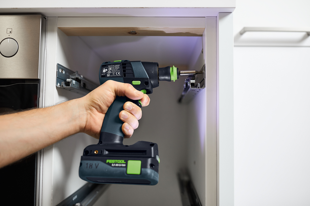 Person using a compact Festool cordless drill to install hardware inside a white cabinet for home improvement tasks