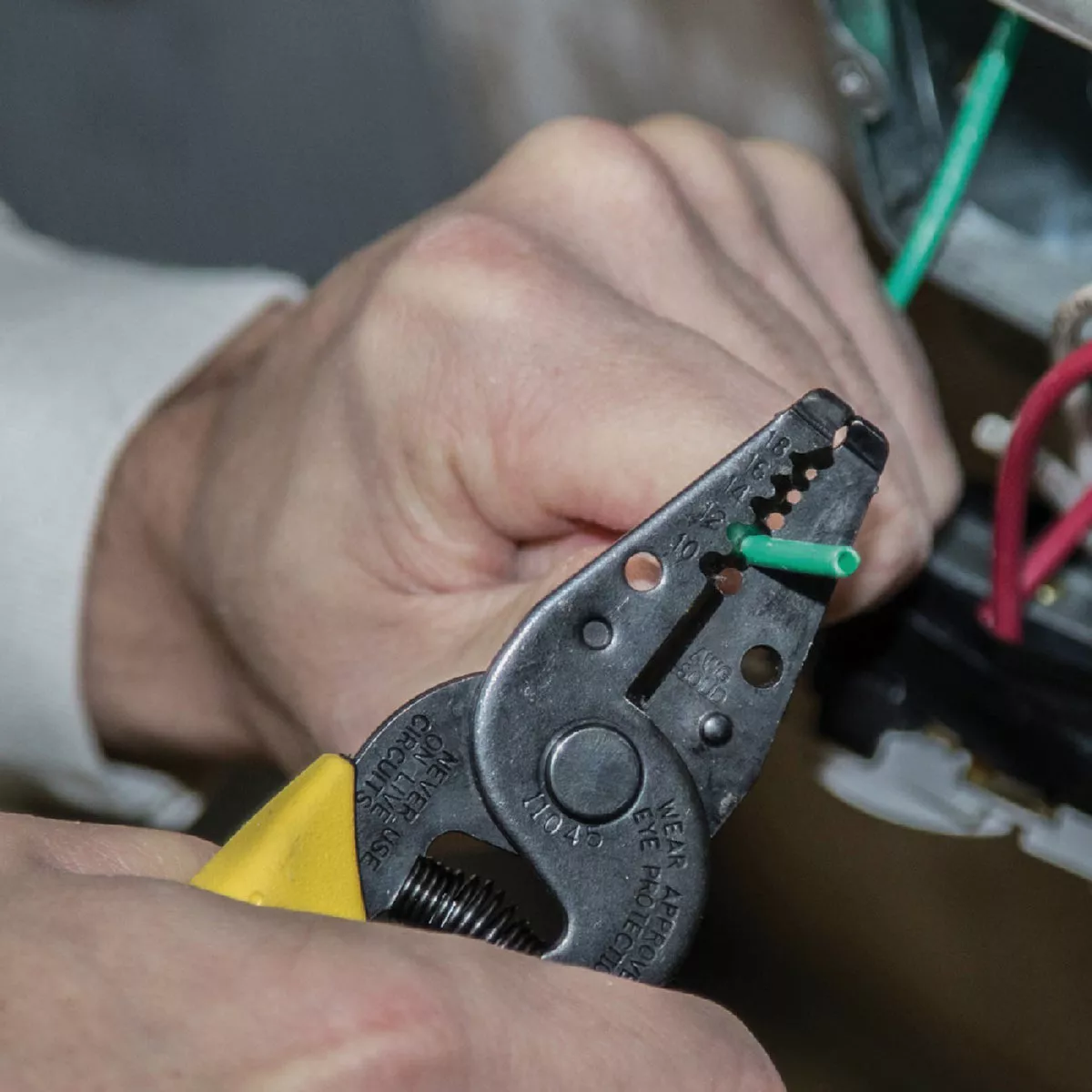 Yellow-handled wire stripper cutting green solid electrical wire for home improvement electrical tools collection