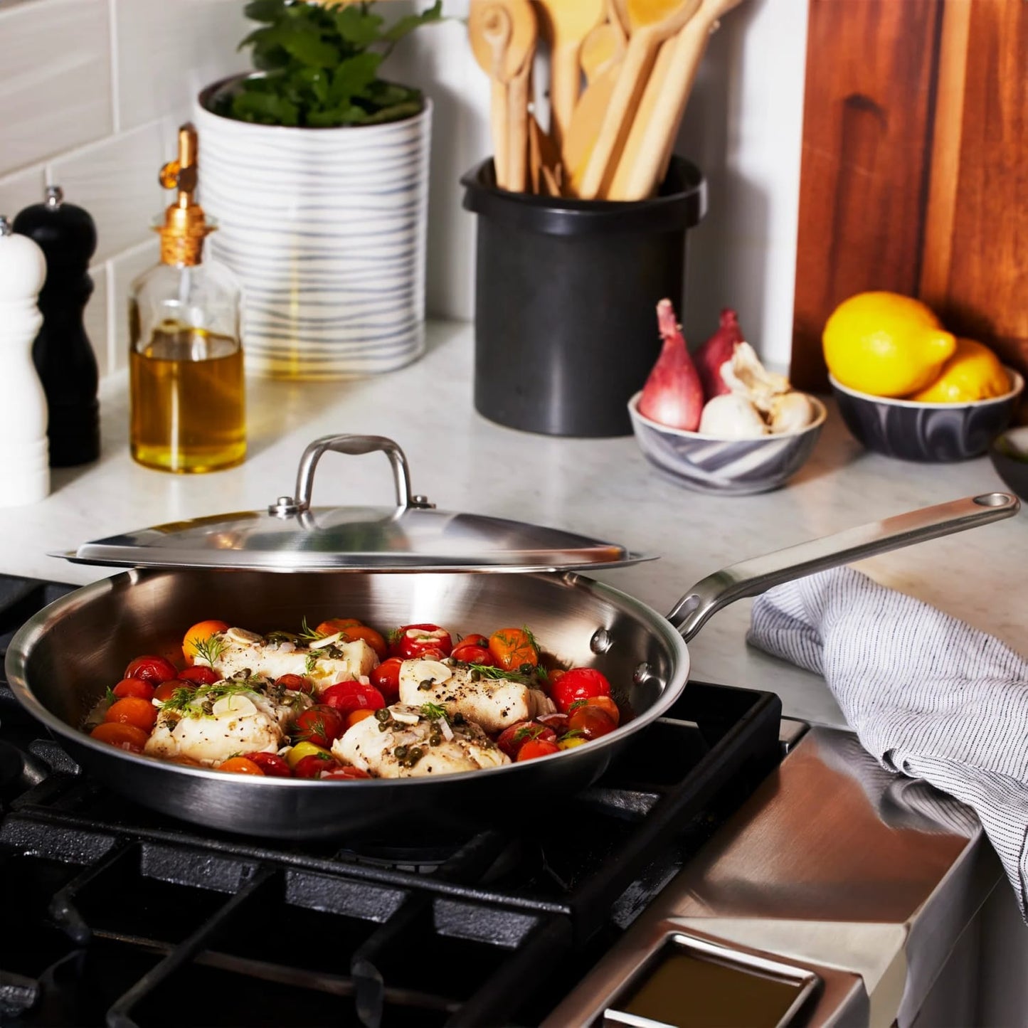 Fully clad stainless steel fry pan cooking chicken and cherry tomatoes on gas stove, kitchenware and home setting.