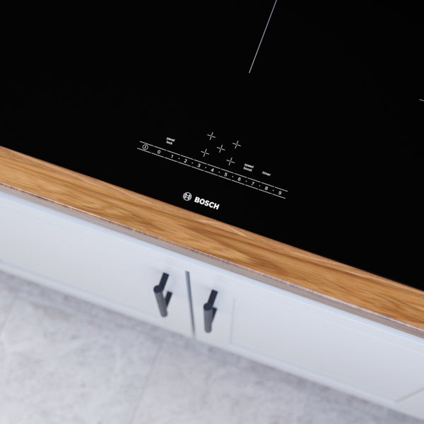 Close-up of black induction cooktop control panel with touch slider and Bosch logo in modern kitchen setting