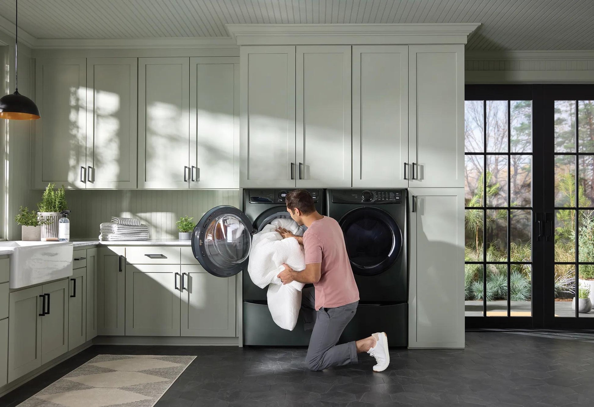 Man loading a dark gray front load gas dryer with laundry in a modern kitchen, part of Dryers and Appliances collections