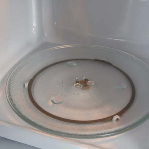 Interior view of microwave oven showing clear glass turntable plate and white microwave cavity in kitchen appliance setting