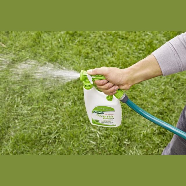 Hand spraying liquid fertilizer from a hose-attached container on a green lawn in lawn care and garden setting