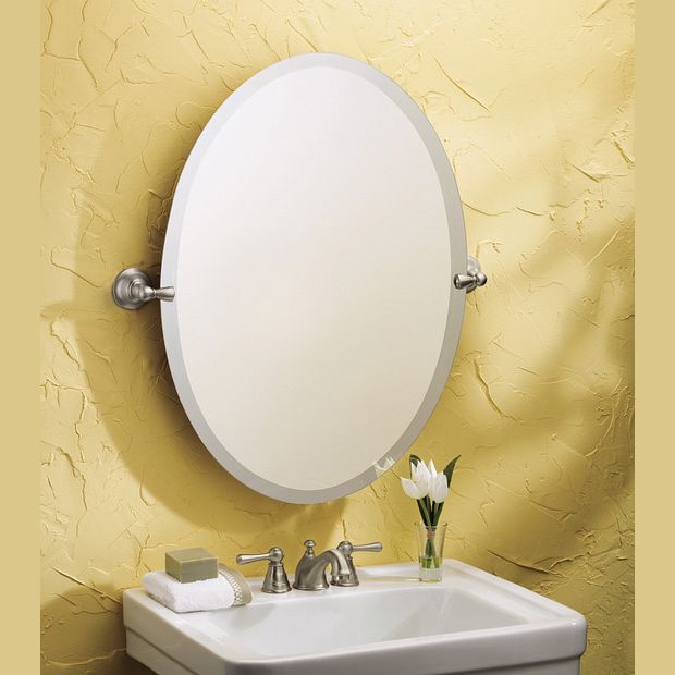 Oval brushed nickel tilting mirror mounted above a white sink with decorative faucet and yellow textured wall backdrop
