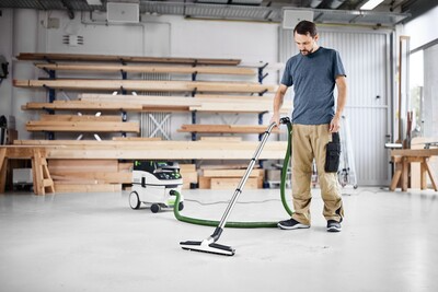 Man using dust extractor with green anti-static hose in bright woodworking shop, dust management and shop vac accessories