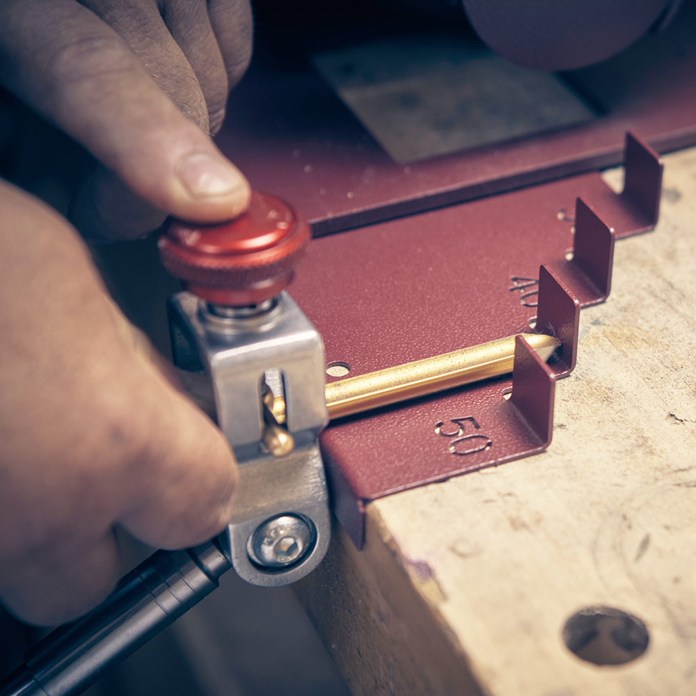 Close-up of red metal jig with brass rod aligned at 50 marking for precise tool sharpening in home improvement tasks