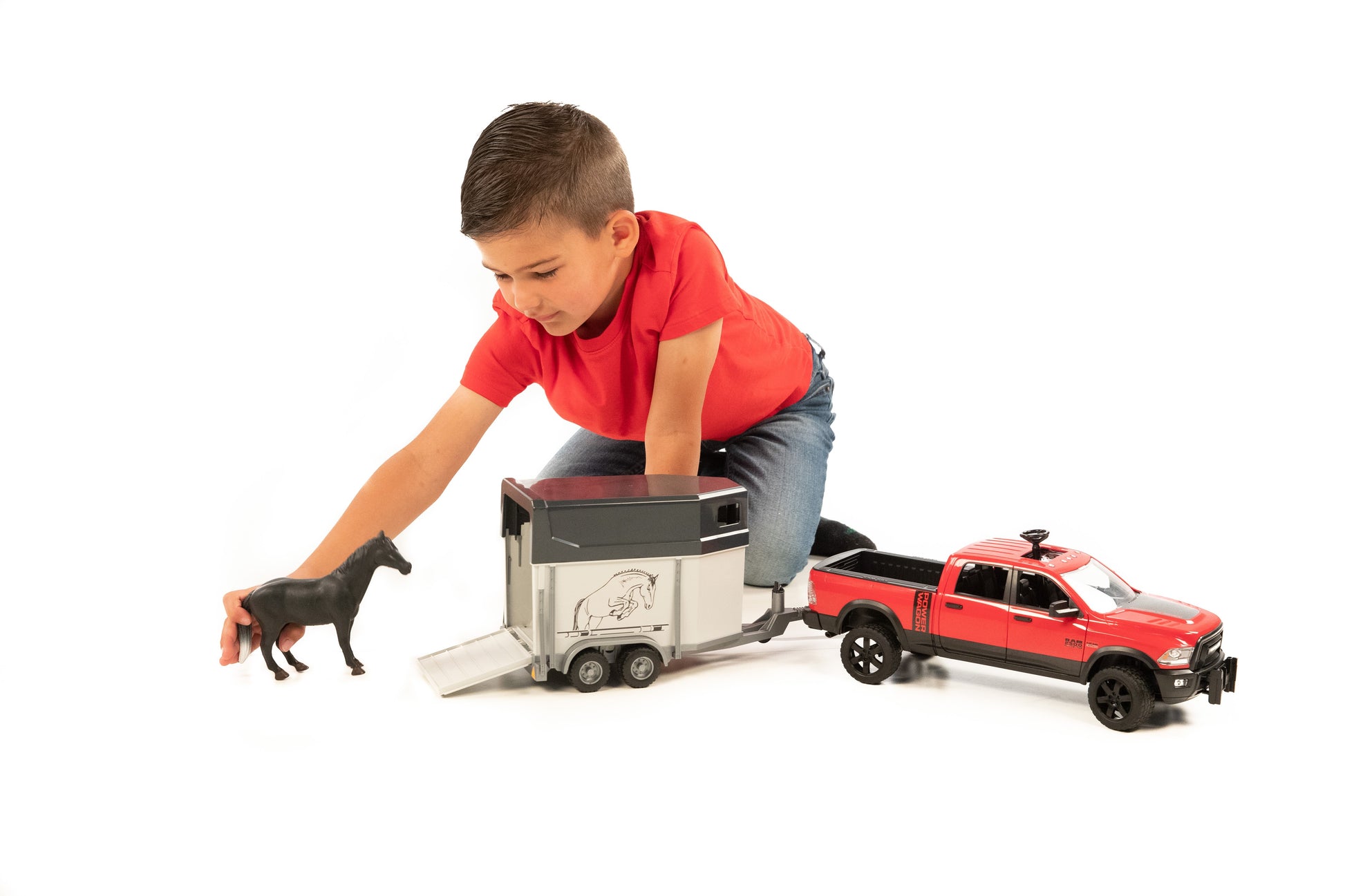 Child playing with red pickup toy and gray horse trailer inserting black horse figure in toys and games collection