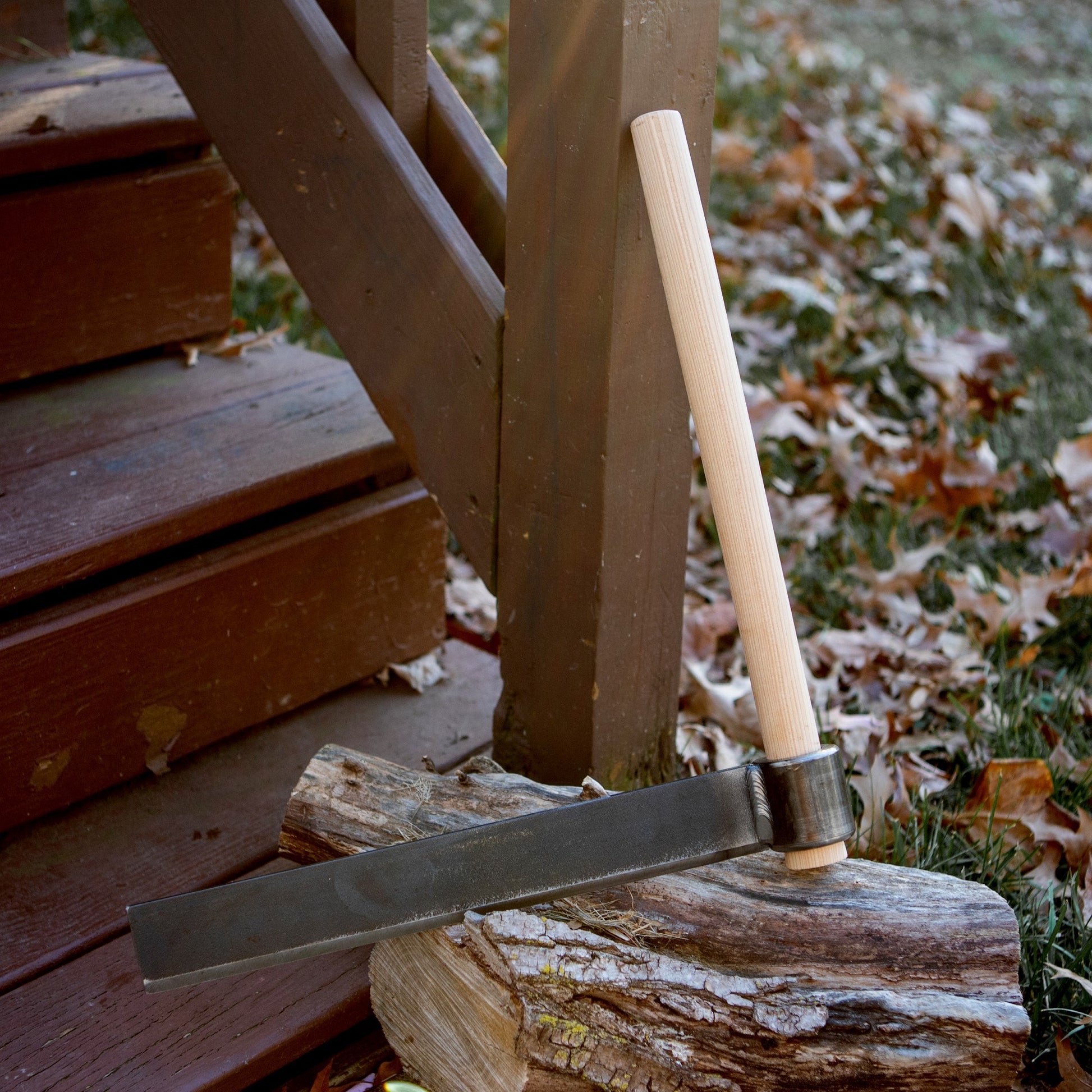 Wood splitting froe with wooden handle resting on a log near outdoor wooden steps, tool accessories collection
