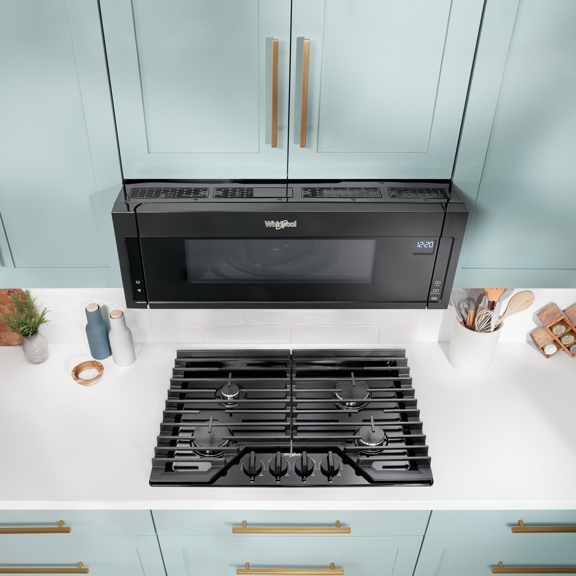 Black Whirlpool over-the-range microwave hood with digital display installed above gas cooktop in modern kitchen setting