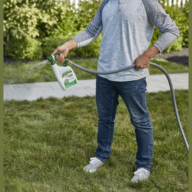 Person using a green and white Scotts liquid turf builder sprayer connected to garden hose for lawn care under $50
