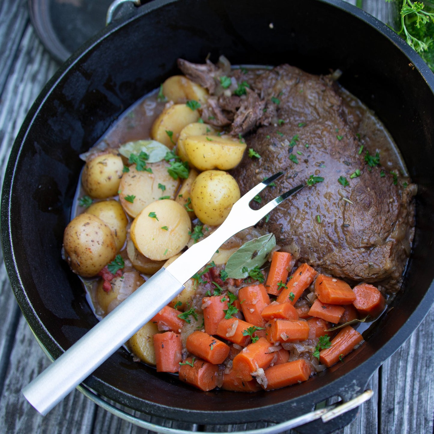 Silver-handled carving fork with two sharp tines resting on pot roast, carrots, and potatoes in cast iron skillet under $50 kitchen utensils