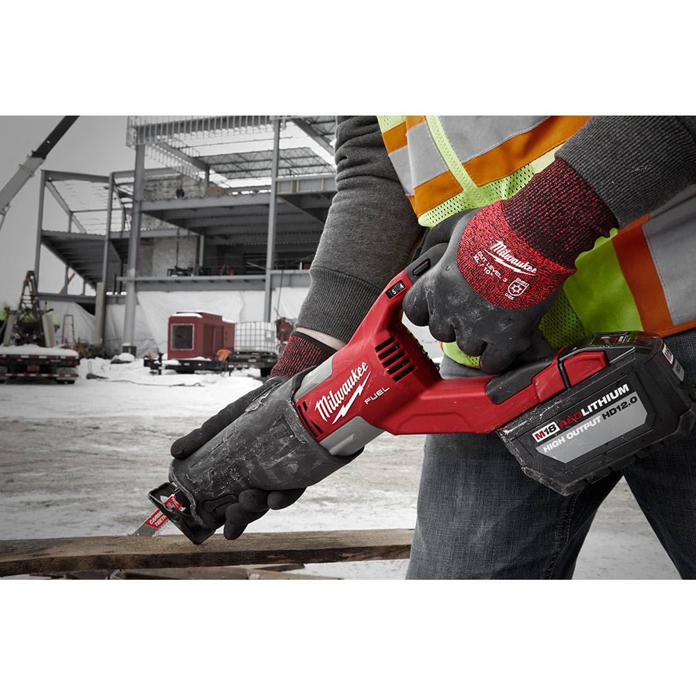 Worker wearing red and black cut-resistant gloves operating a red Milwaukee cordless reciprocating saw outdoors