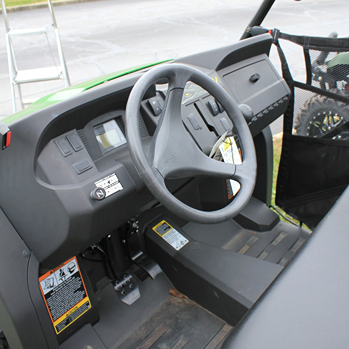 Interior view of a utility vehicle cabin with steering wheel, dashboard controls, and foot pedals for outdoor use