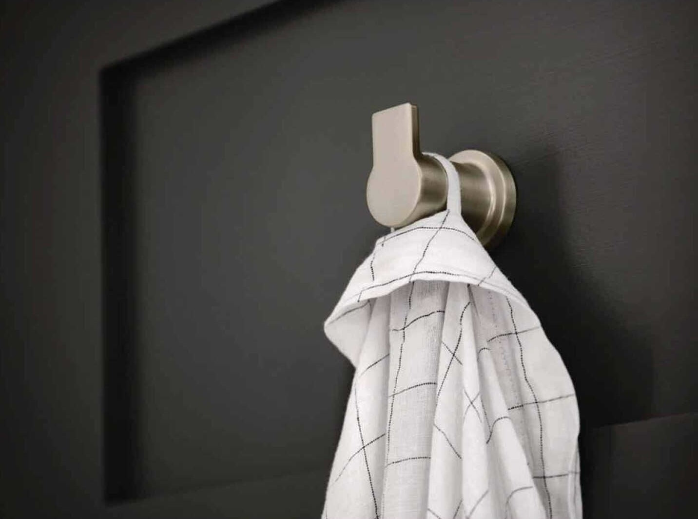 Brushed metal wall hook holding a white kitchen towel with black grid pattern on dark background