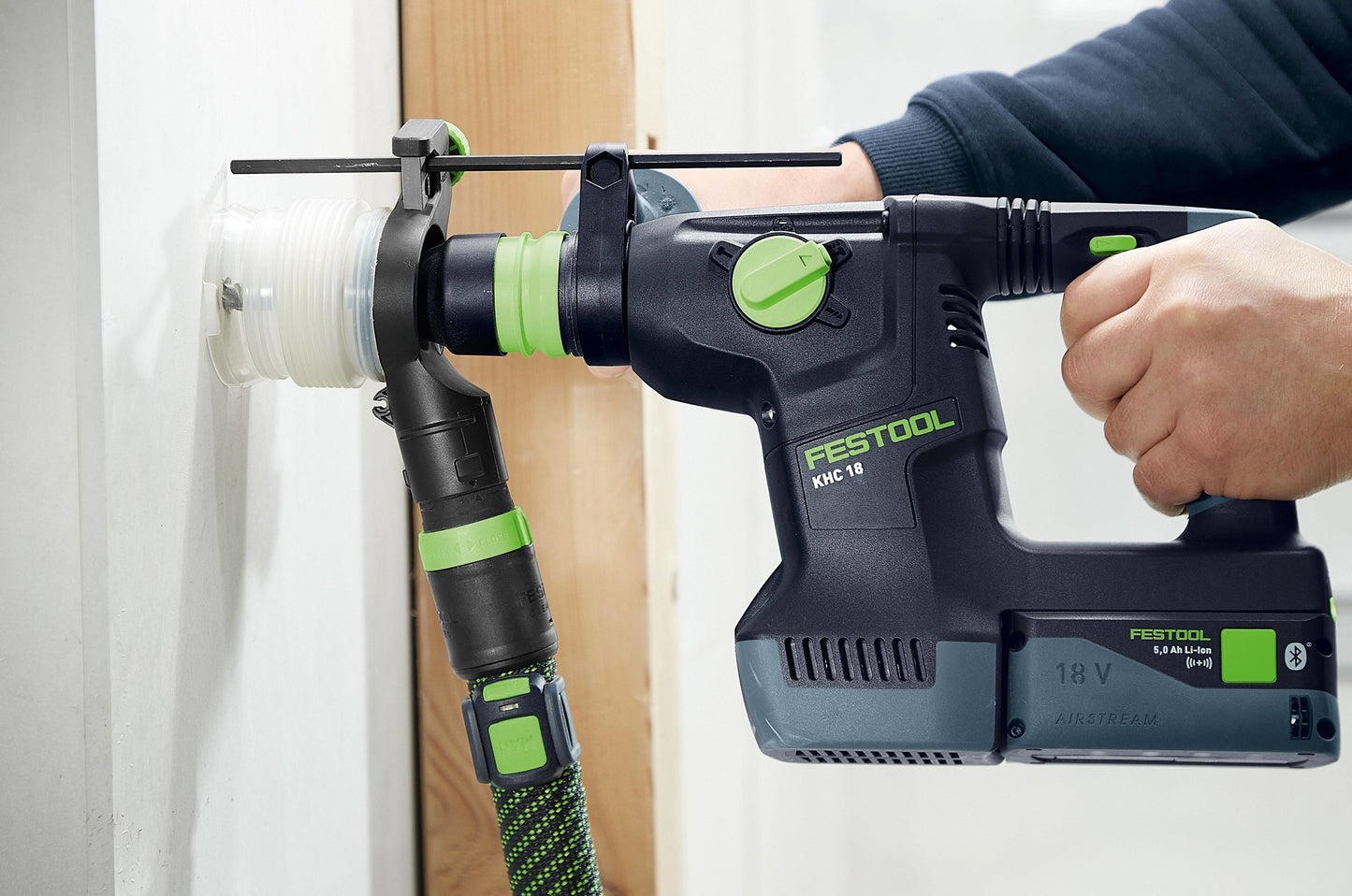 Compact black and green cordless drill with attached dust extraction hose for clean home improvement work