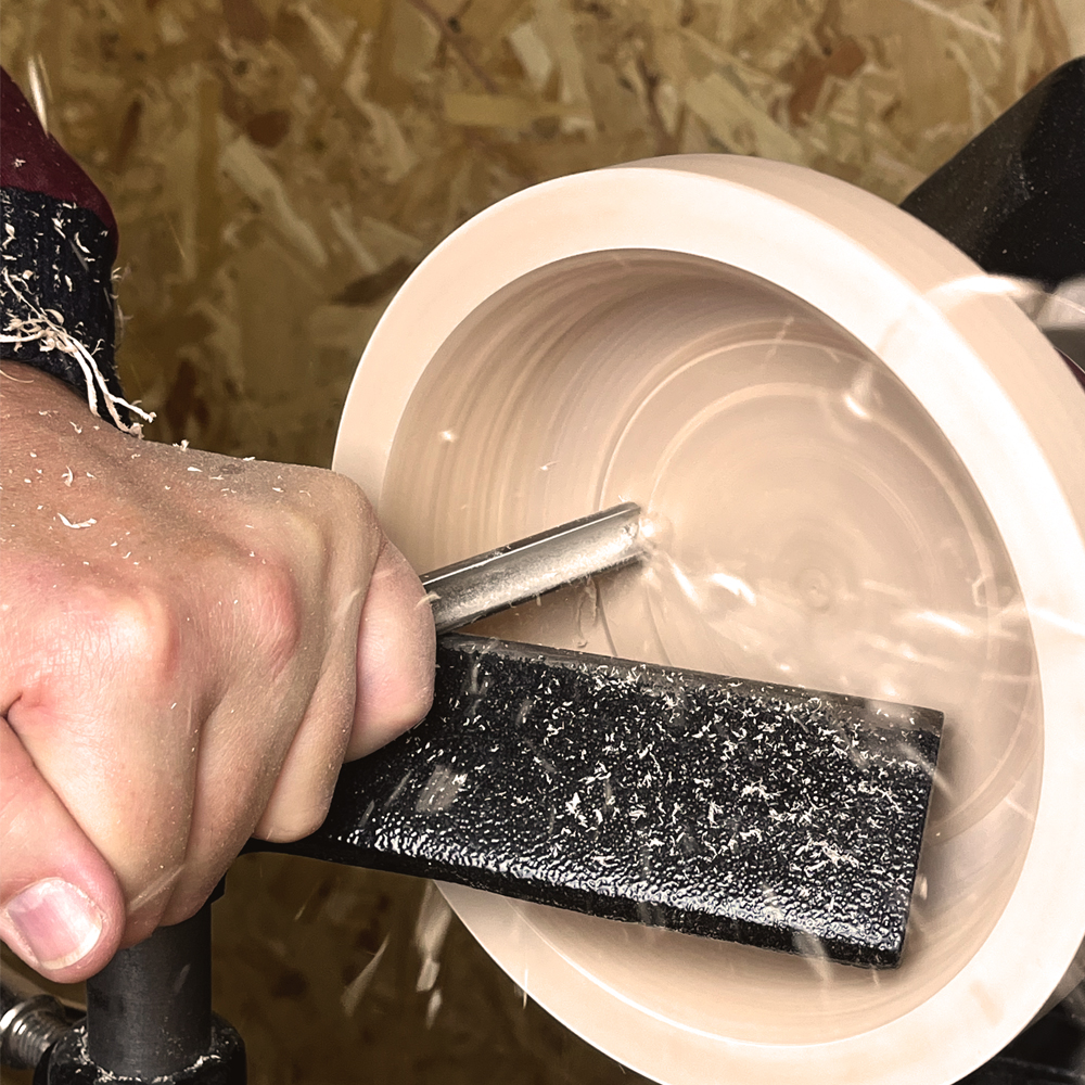 Close-up of a hand using a steel bowl turning tool to shape a spinning wooden bowl on a lathe for home improvement tasks
