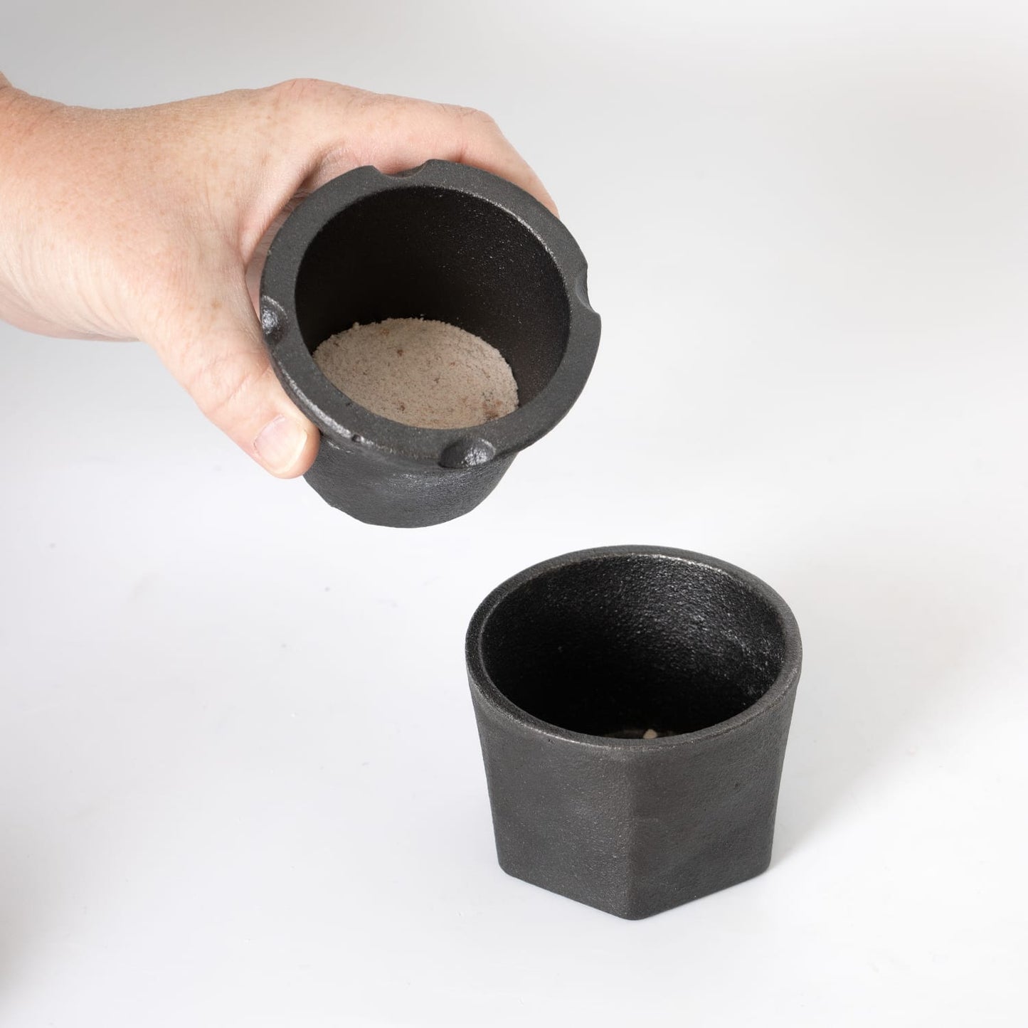 Hand holding black cast iron spice grinder with ground salt inside and matching bottom piece on white surface under $50 kitchenware