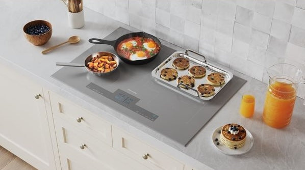 Titanium gray induction cooktop with frying pan and baking sheet on white countertop, part of Thermador cooktops collection