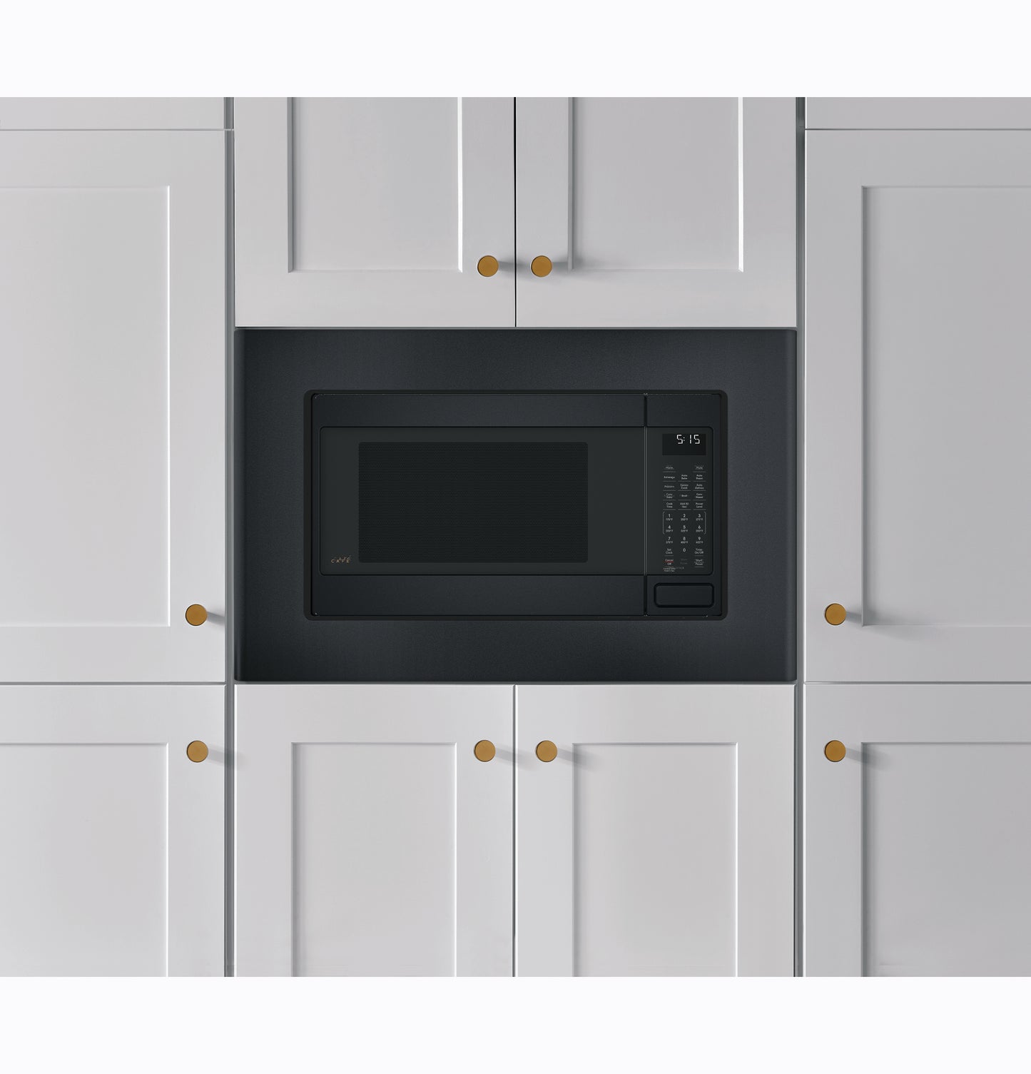 Built-in black trim kit framing a microwave installed in white kitchen cabinetry with brass knobs in appliances collection