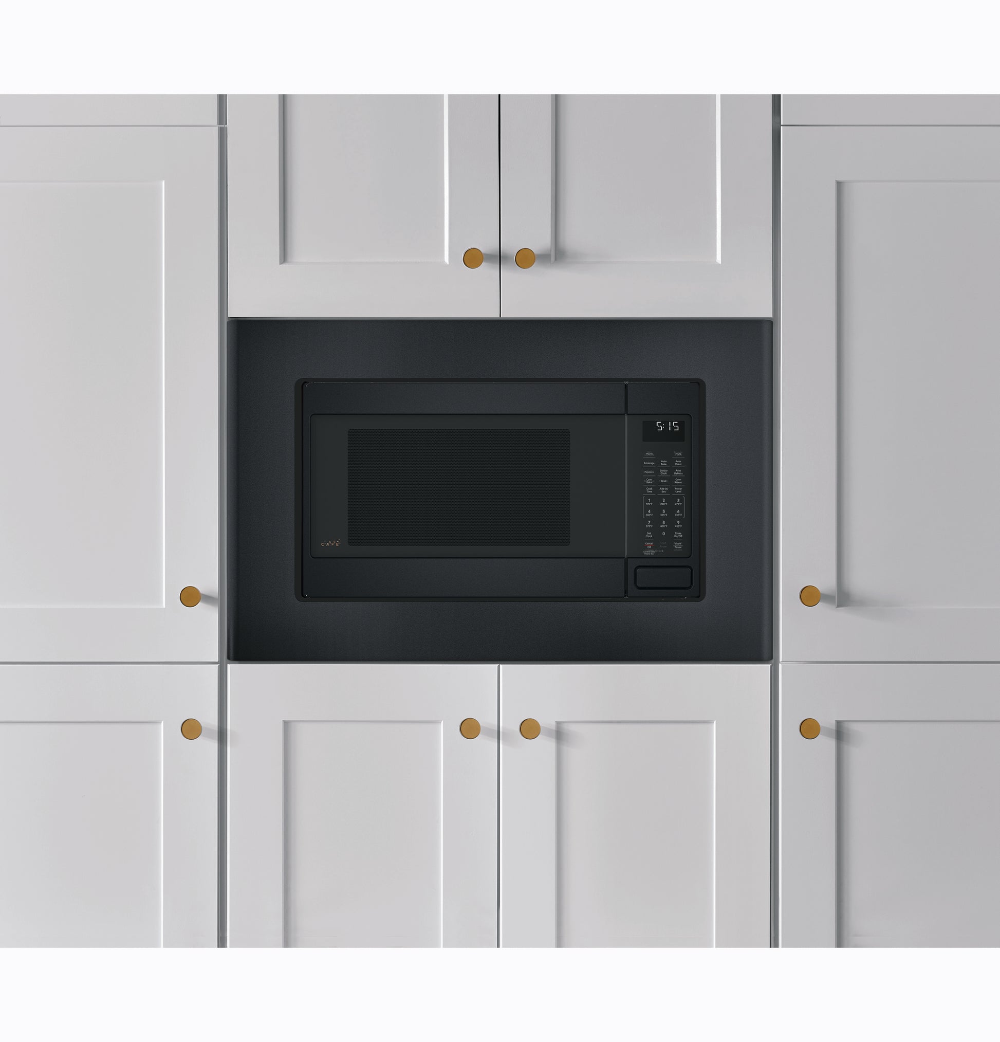 Built-in black trim kit framing a microwave installed in white kitchen cabinetry with brass knobs in appliances collection