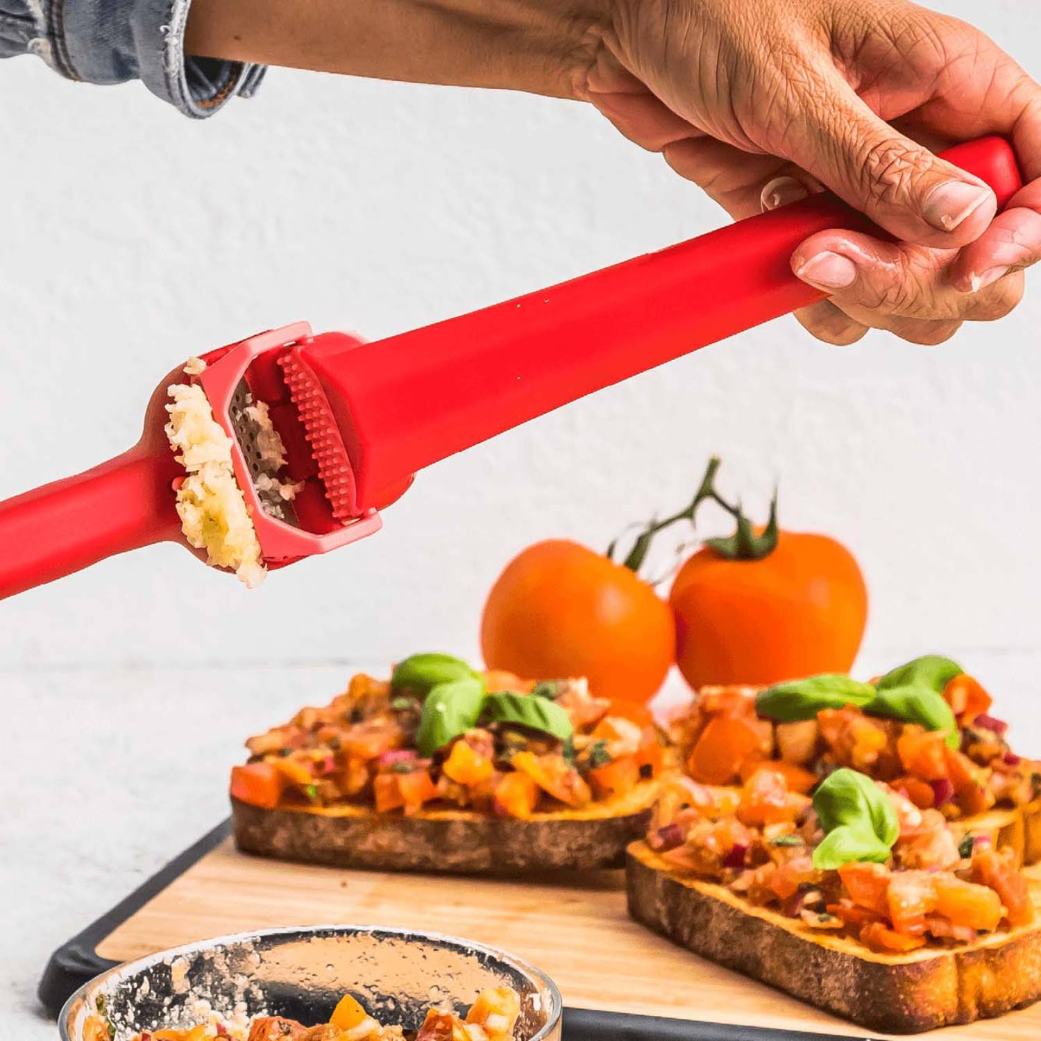 Red garlic press crushing fresh garlic with peel ejector over appetizer toast in kitchenware and cooking utensils collections