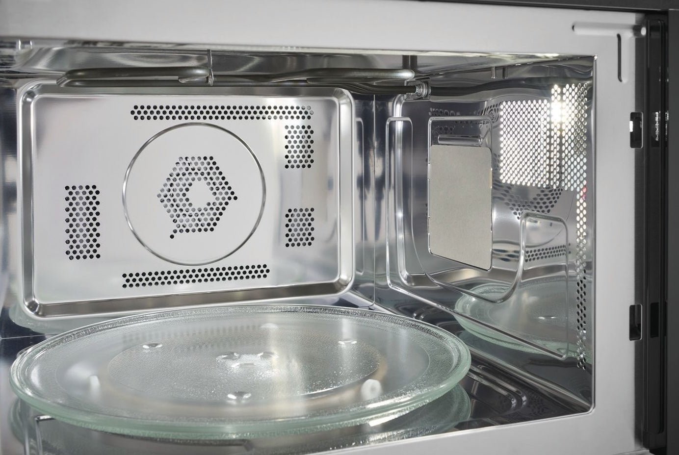 Interior view of stainless steel built-in microwave oven with glass turntable and ventilation perforations