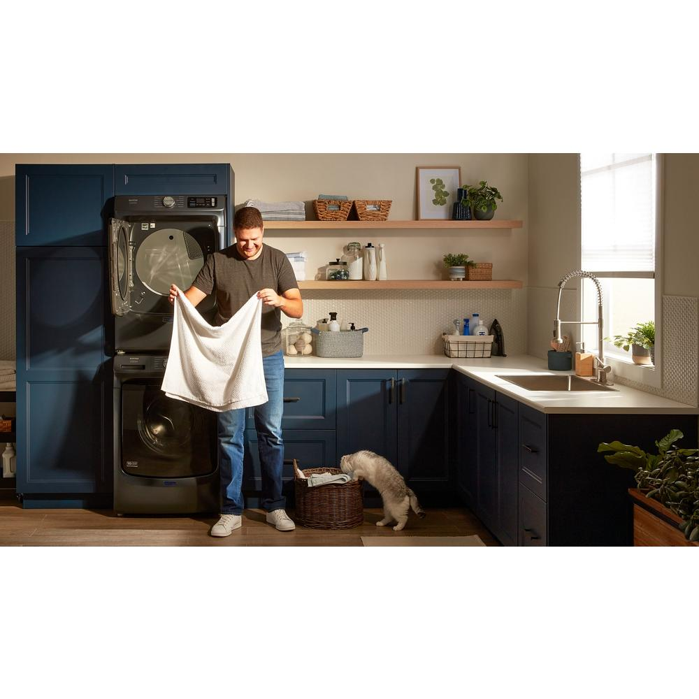 Man loading laundry into dark front load washer in modern kitchen with blue cabinets and pet nearby