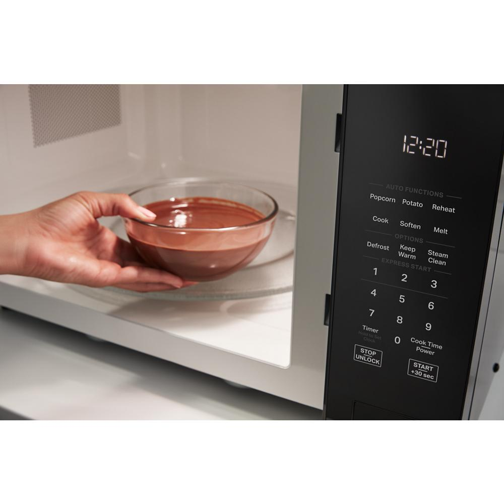 Hand placing glass bowl with food inside a microwave showing digital control panel and keypad for kitchen use