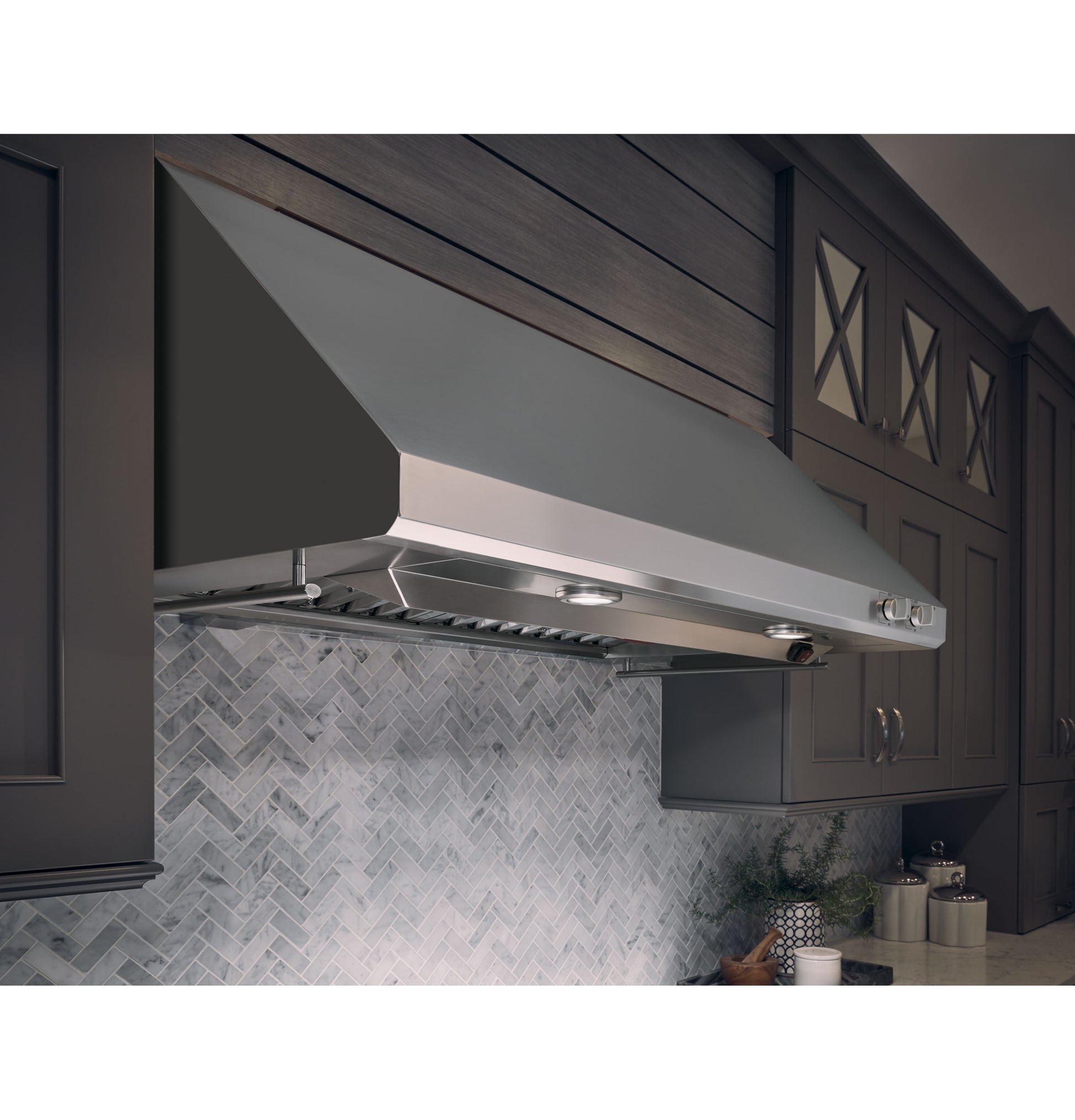Stainless steel professional kitchen hood installed above countertop with gray cabinetry and tiled backsplash in Appliances collections