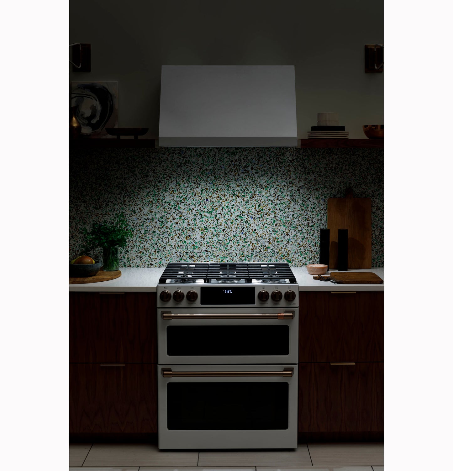 Modern kitchen setup with stainless steel stove and a sleek white commercial hood over a terrazzo backsplash