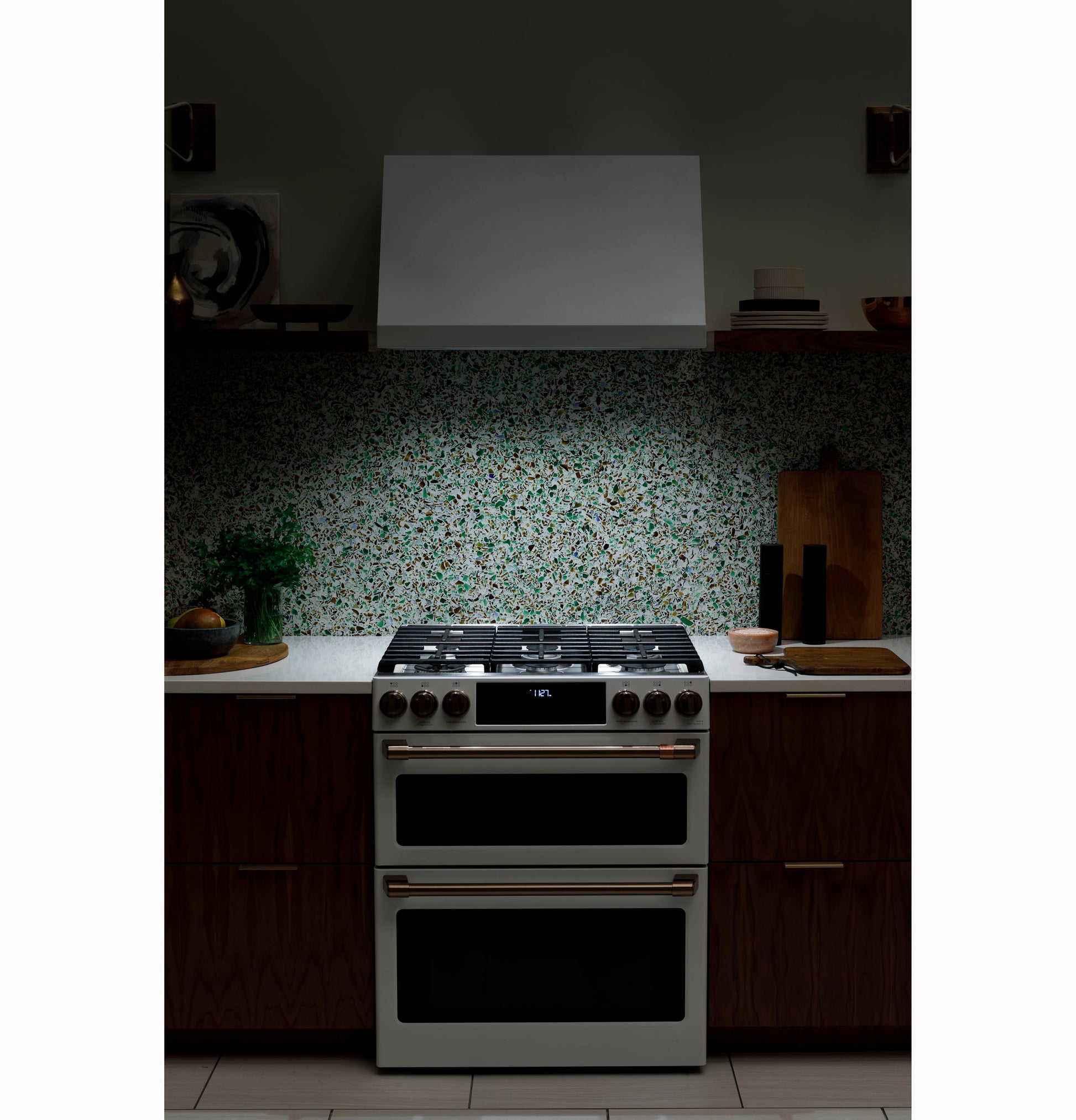 Modern kitchen setup with stainless steel stove and a sleek white commercial hood over a terrazzo backsplash