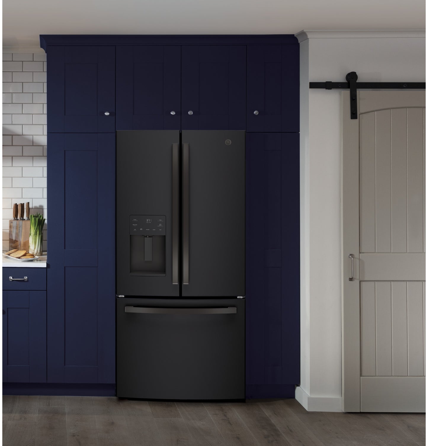 Black French-door refrigerator with bottom freezer integrated into modern navy blue kitchen cabinetry next to a sliding barn door