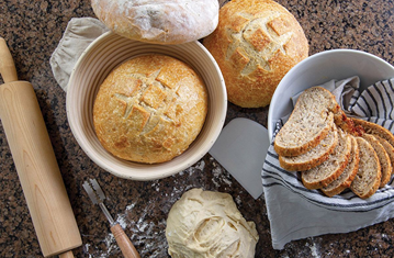 Freshly baked artisan bread loaves and sliced loaf on kitchenware with rolling pin and bread lame tools under $50 collections