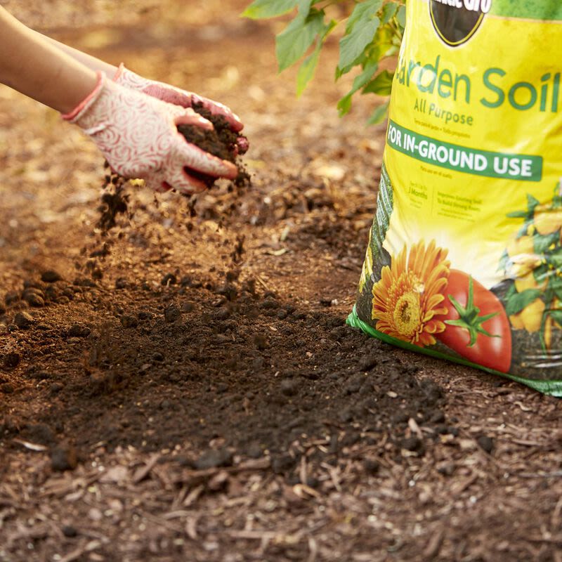 Hands in pink patterned gloves spreading soil next to a bright bag of garden soil for outdoor living projects