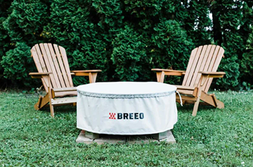 Light gray Breeo fire pit cover protecting fire pit, set among wooden Adirondack chairs in outdoor home setting