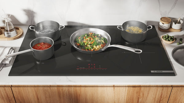 Black induction cooktop with four pots and pans cooking various dishes from Bosch Appliances collection