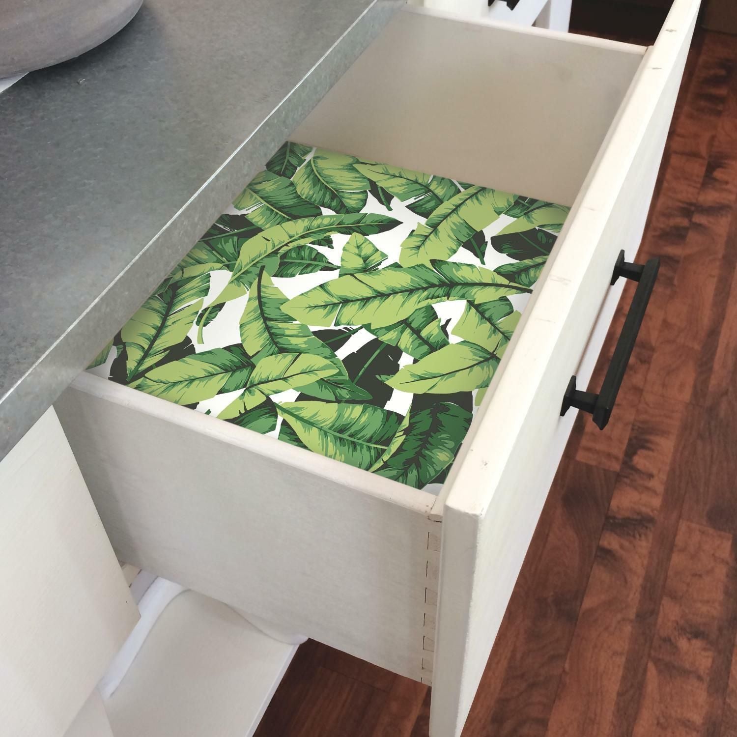Open white drawer lined with green palm leaf peel and stick wallpaper for home organization and decor