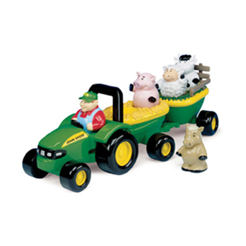 Green toy tractor with yellow wheels pulling a trailer carrying plastic farm animals and a driver figure