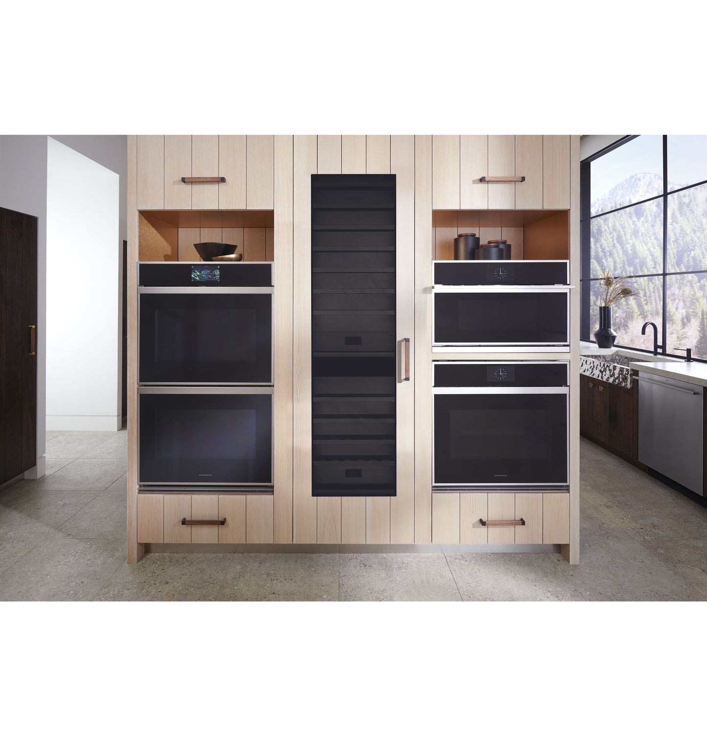 Built-in panel-ready wine column with black glass door, flanked by stainless steel ovens in a modern kitchen setting.