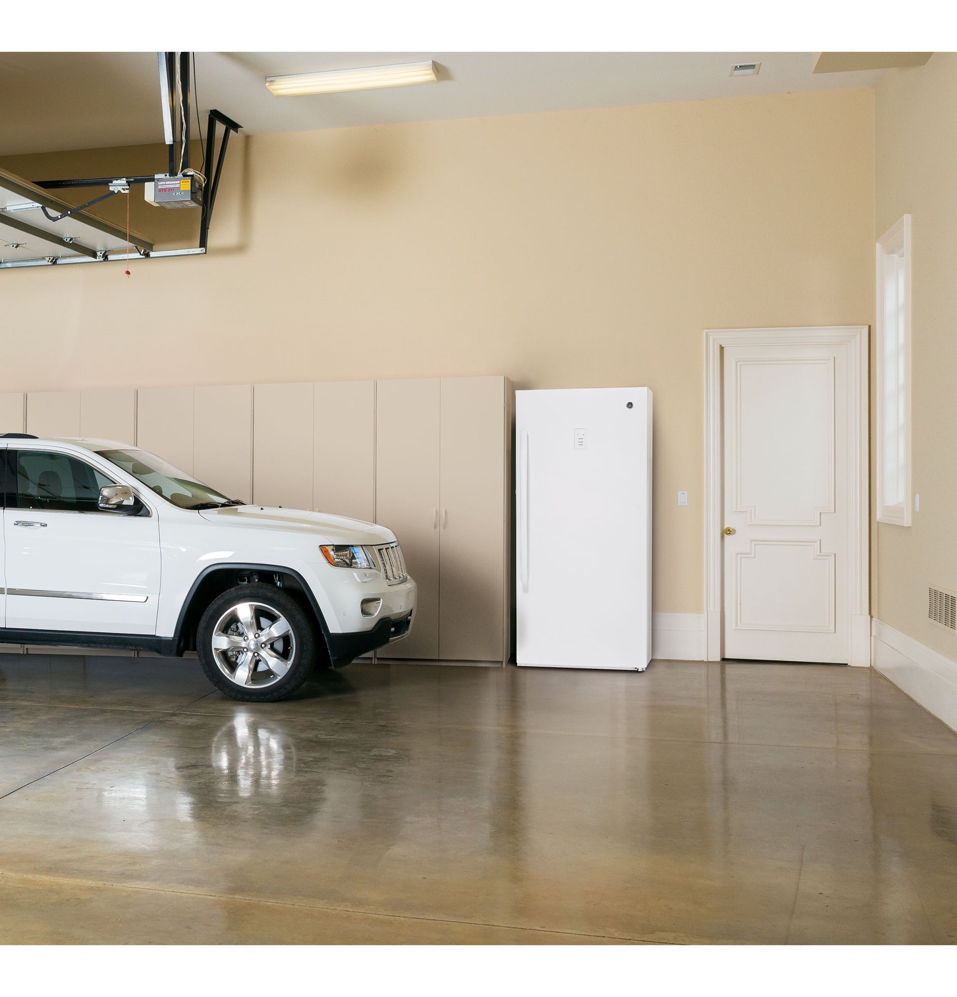 White frost-free upright freezer with vertical handle installed in spacious beige garage with white SUV and storage cabinets