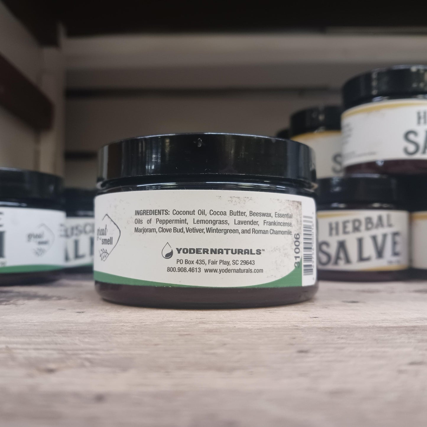 Small jar of Yoder Naturals muscle balm showing ingredients label with natural oils and herbs on wooden surface
