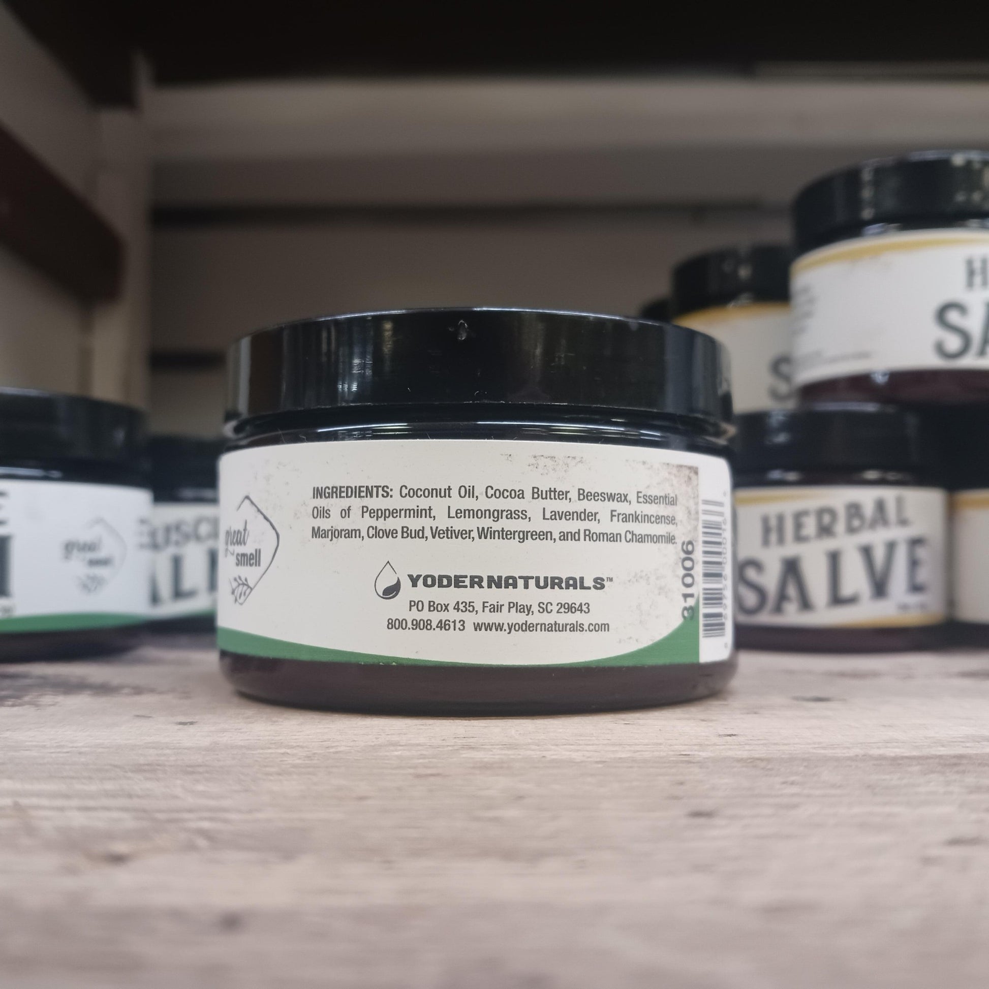 Small jar of Yoder Naturals muscle balm showing ingredients label with natural oils and herbs on wooden surface