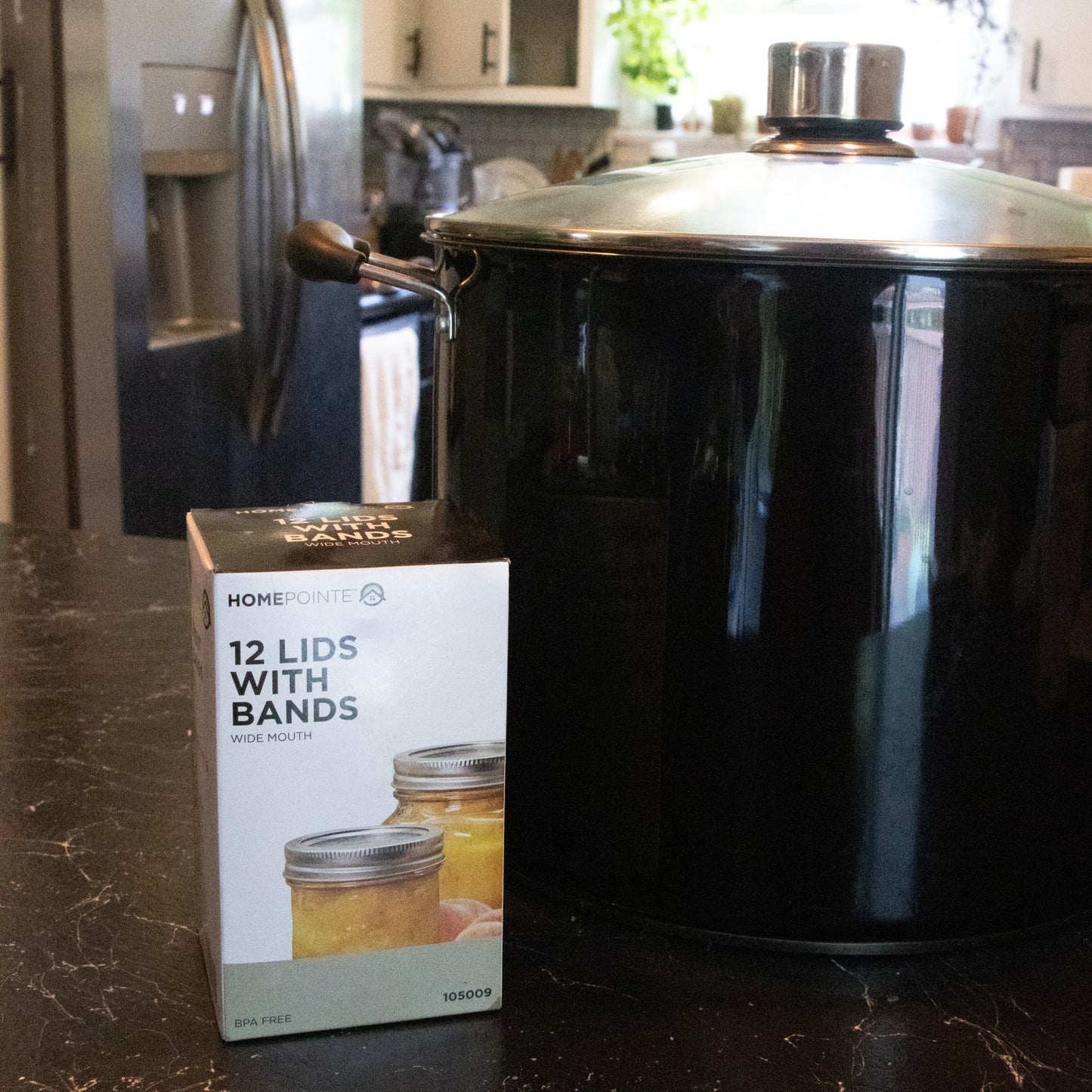 Box of 12 wide-mouth jar lids and bands displayed beside a large black pot on a kitchen countertop, suitable for kitchenware and under $50 collections