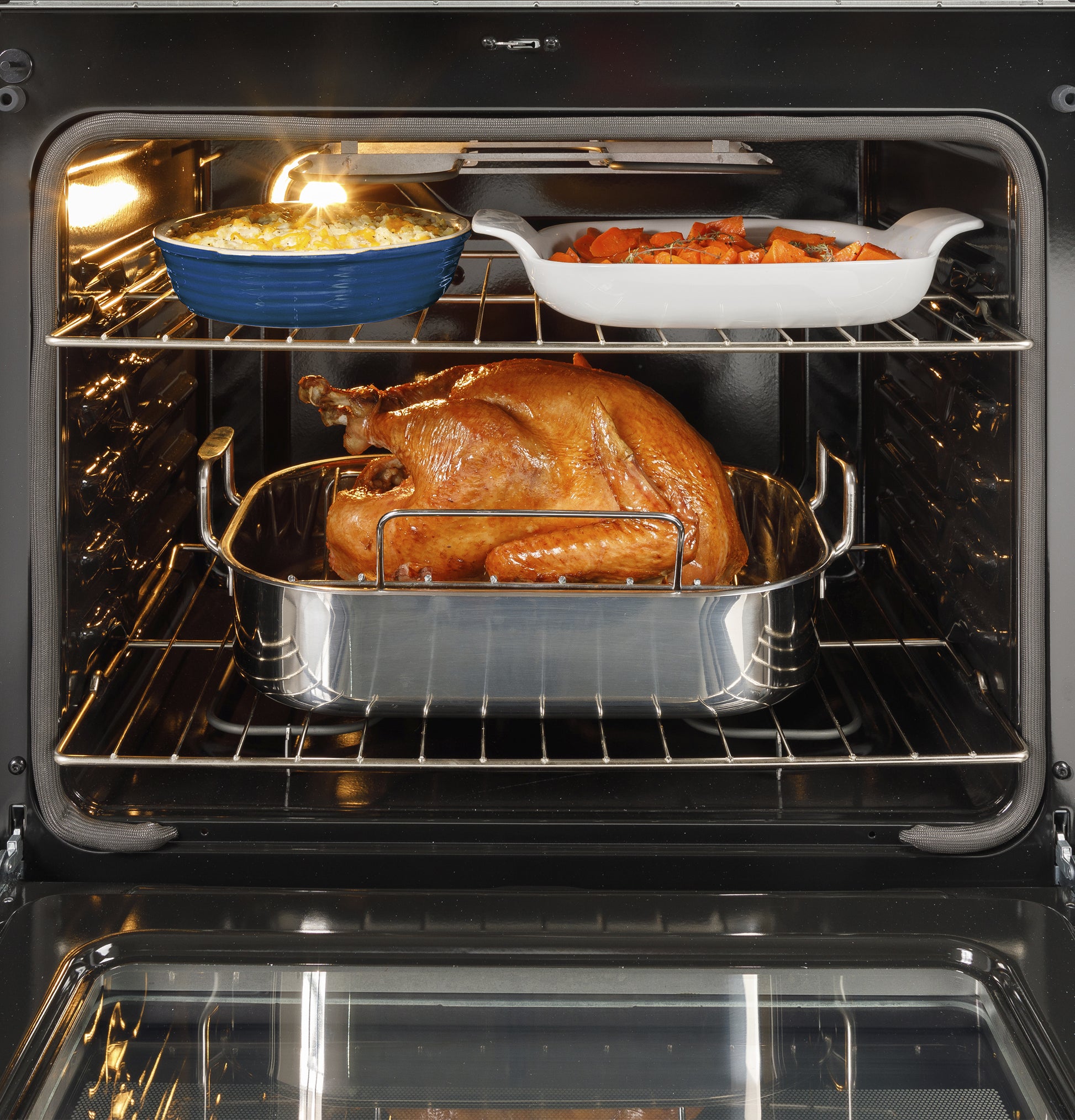 Roast turkey cooking in a stainless steel pan with side dishes in ceramic bakeware inside a kitchen oven