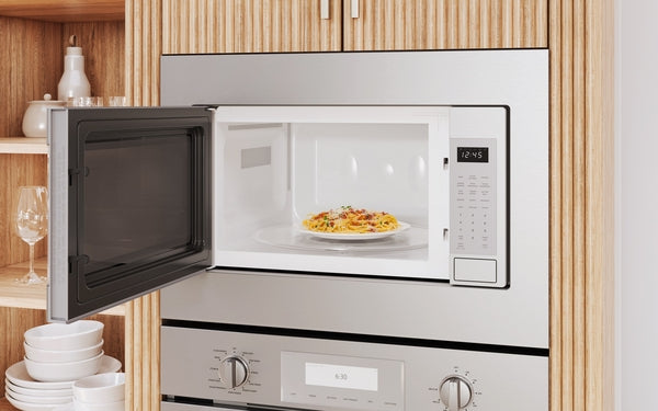Built-in stainless steel microwave with left side door open, showing interior with plate of pasta and digital control panel