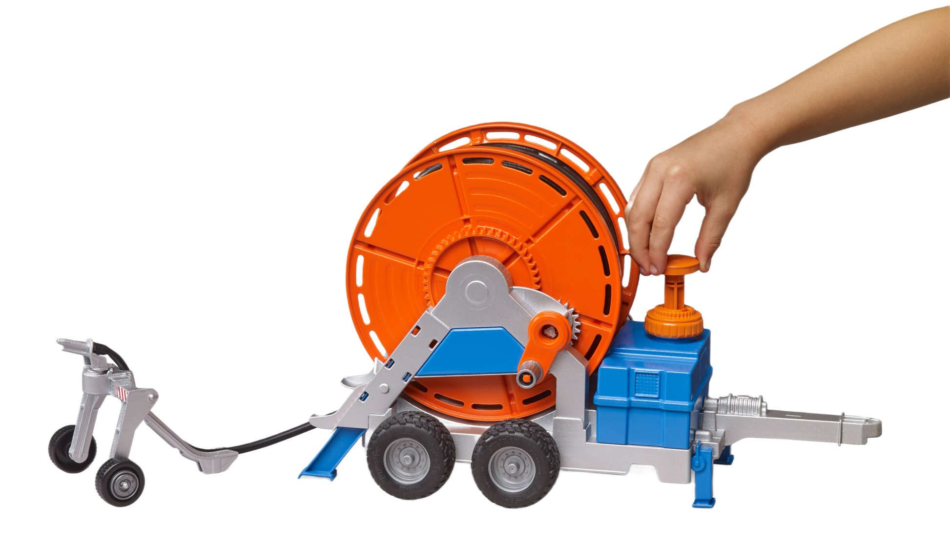 Hand interacting with toy irrigation trailer featuring bright orange reel and blue-gray frame from Bruder Toys collection