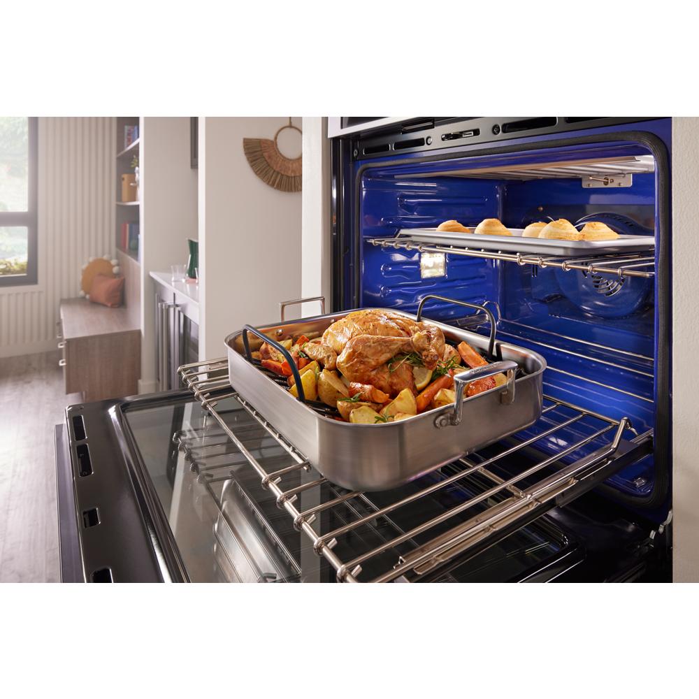 Open wall oven with roasted chicken and vegetables on lower rack and bread rolls baking on upper rack in kitchen setting